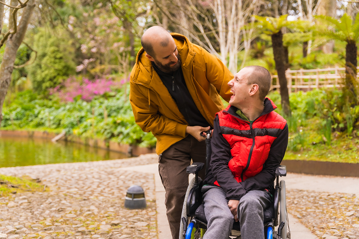 A support worker walking outdoors with a client who uses a wheelchair